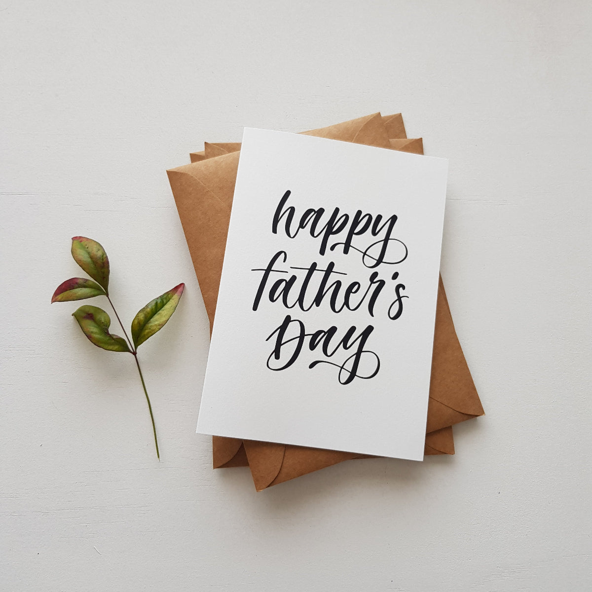 Greeting card with script in black 'happy fathers day' on brown kraft envelopes with leaves