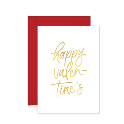 A white greeting card with 'happy valentine's' written in gold script, shown with a red envelope on a white background.