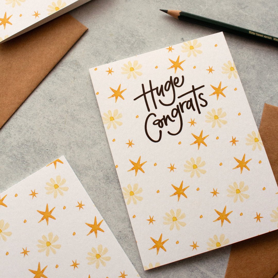 Huge Congrats congratulations card featuring flowers and stars, styled with a pencil and envelopes. 