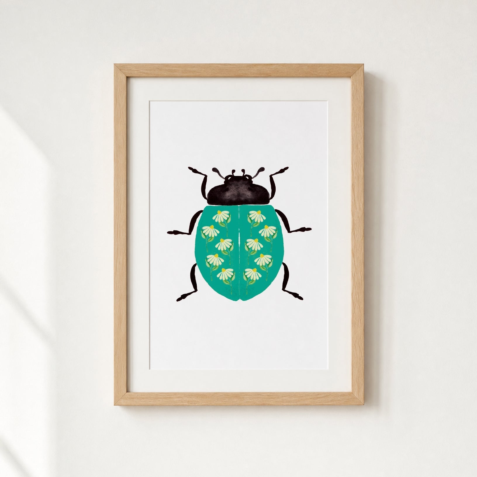 Framed artwork of a teal ladybug with daisies on a white wall.