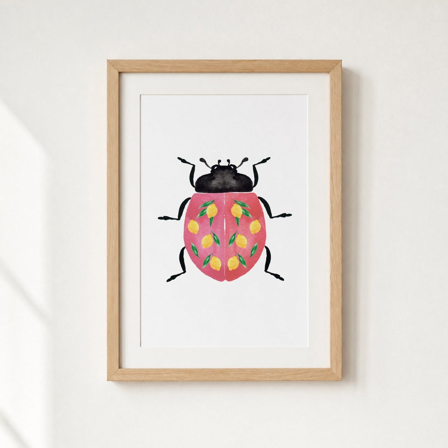 Framed artwork of a ladybug with a pink shell and yellow lemons on a white wall.