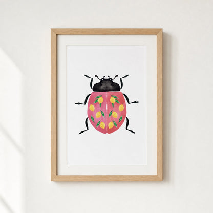 Framed artwork of a ladybug with a pink shell and yellow lemons on a white wall.