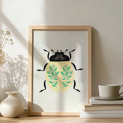 Framed artwork of a beetle with floral design on a table with a cup and books.