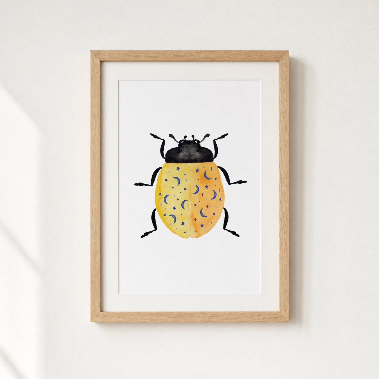 Framed artwork of a yellow beetle with blue moons and stars on a white wall.