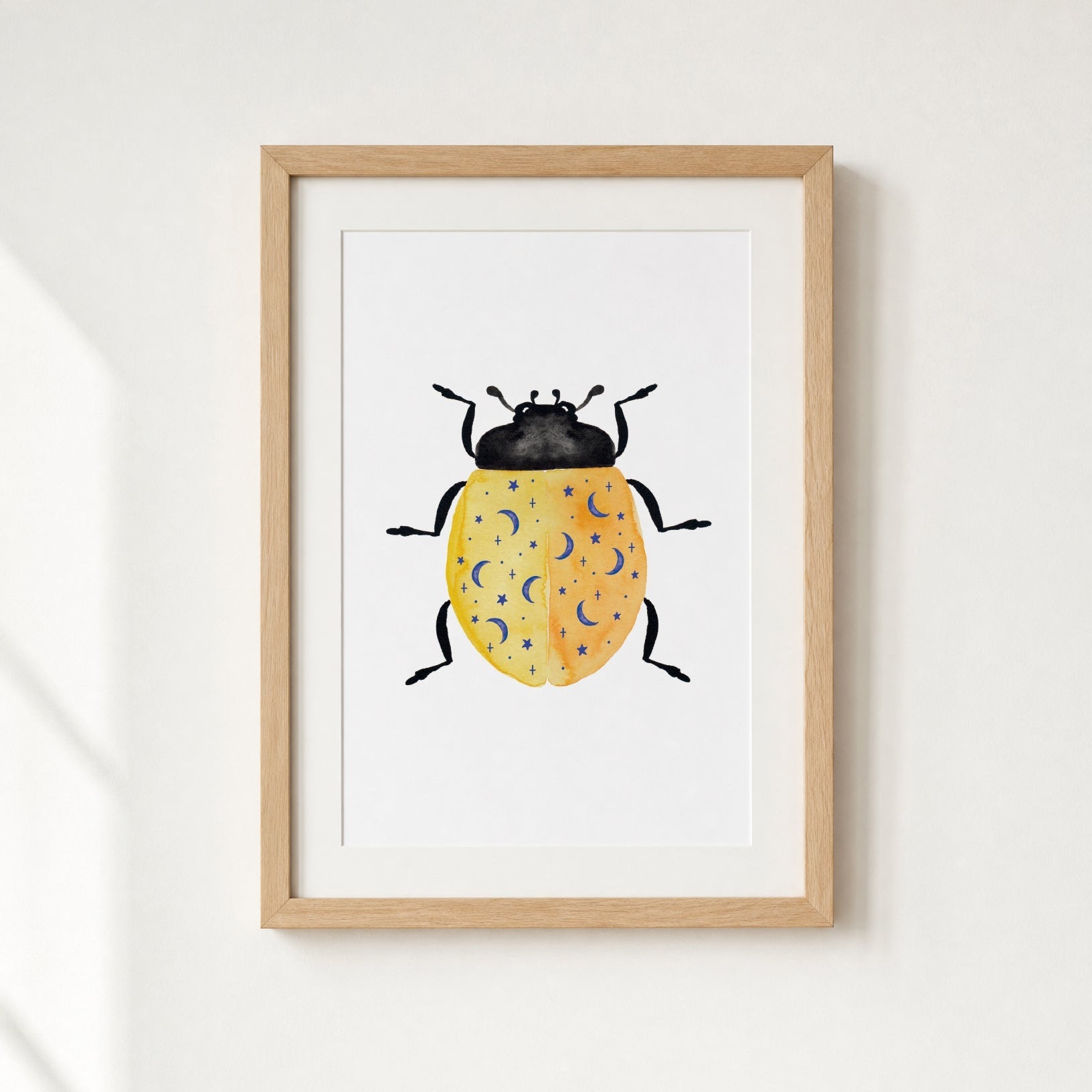 Framed artwork of a yellow beetle with blue moons and stars on a white wall.