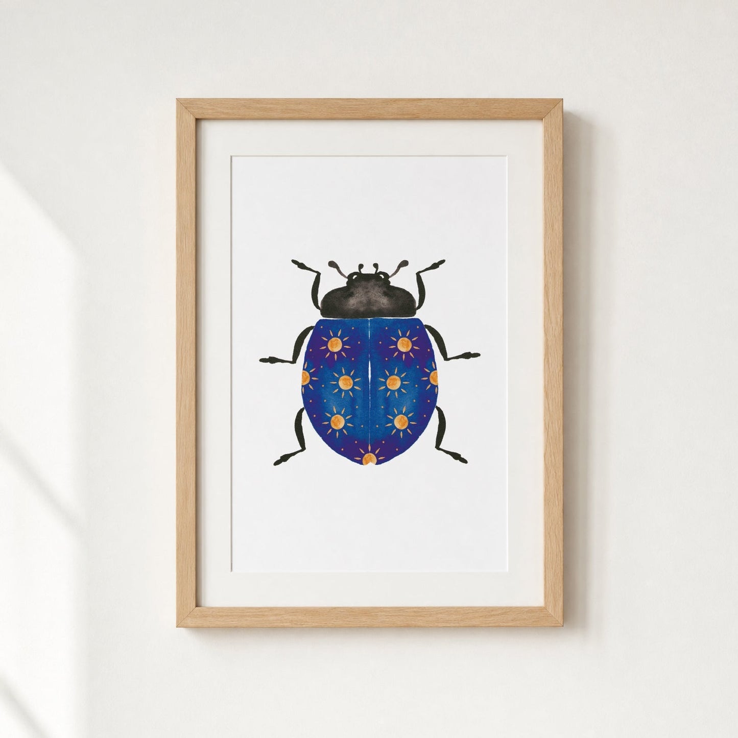 Framed artwork of a blue beetle with yellow suns on a white wall