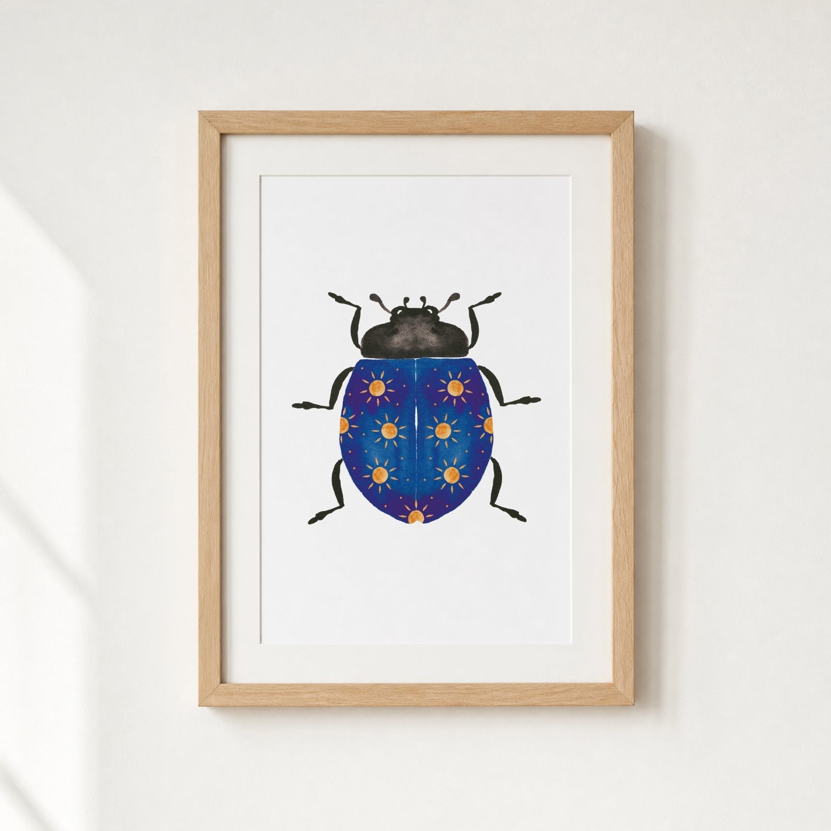Framed artwork of a blue beetle with yellow suns on a white wall