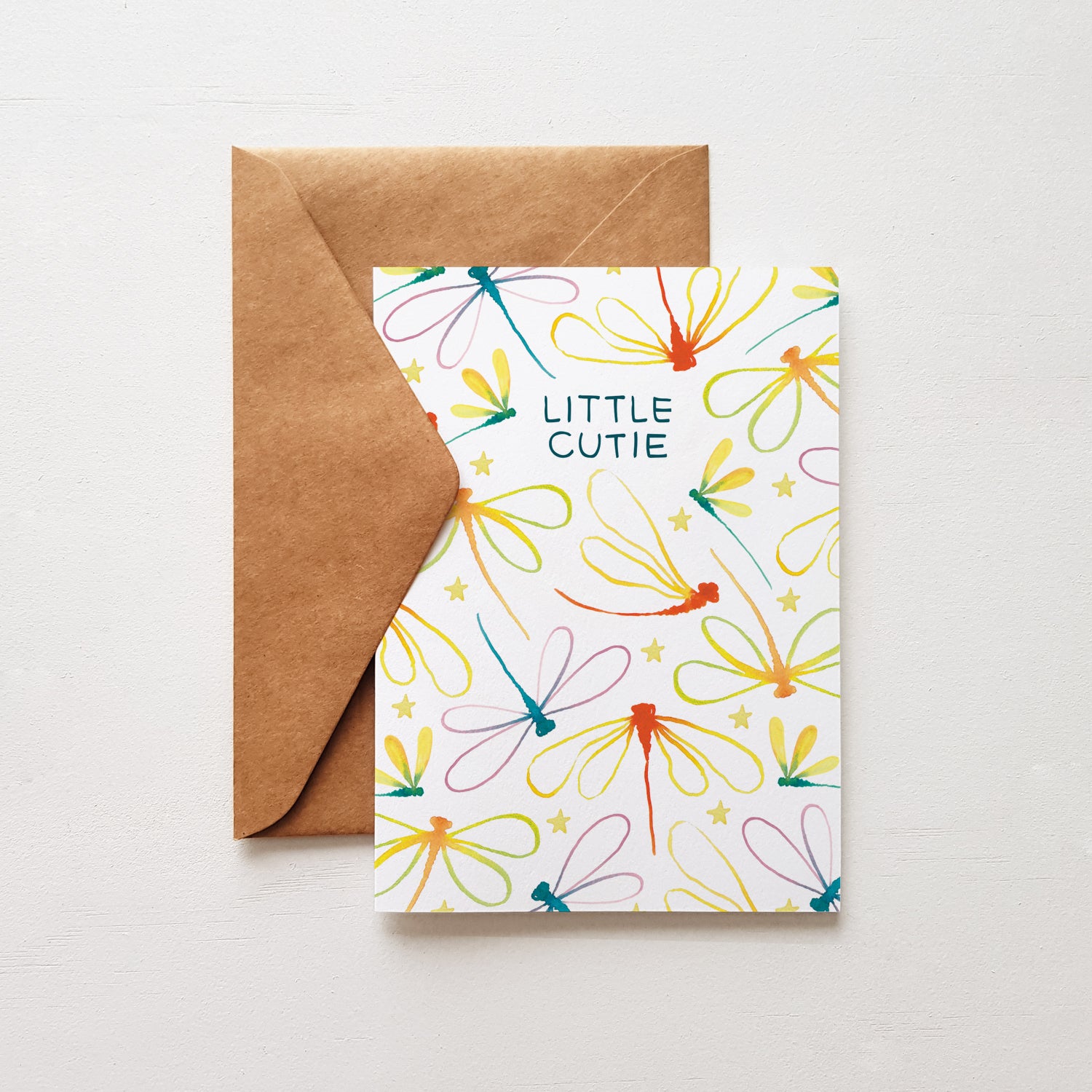 Baby card with the words 'little cutie' surrounded by rainbow dragonflies with a brown envelope