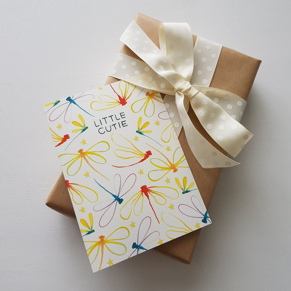 rainbow dragonfly baby card ontop of a brown present with a cream ribbon