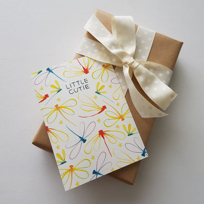 rainbow dragonfly baby card ontop of a brown present with a cream ribbon