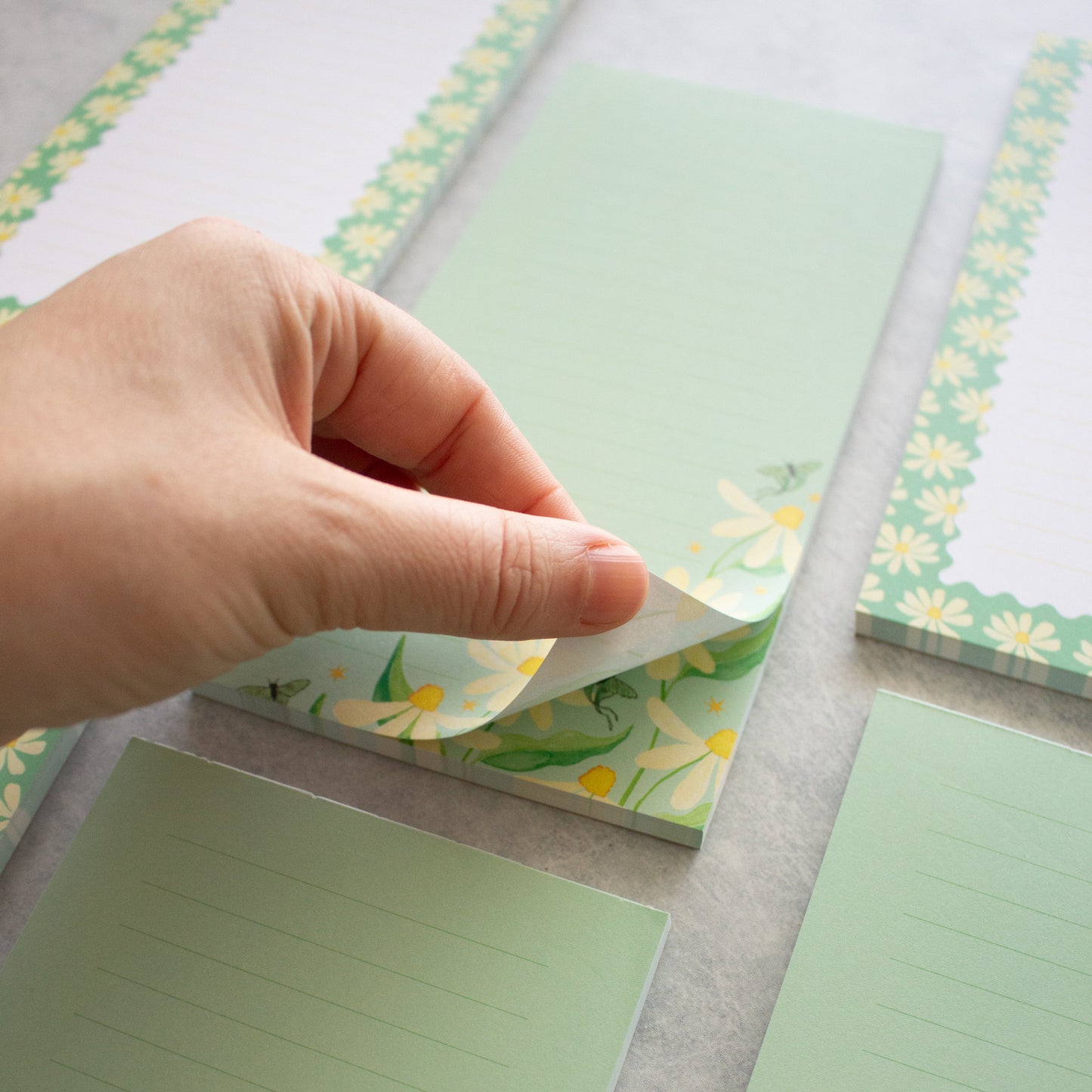 Hand holding a green notepad with floral design on a grey surface