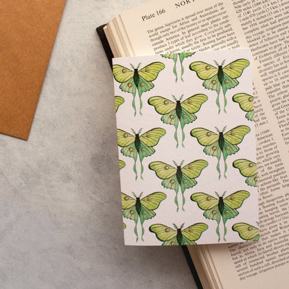 Greeting card with green and teal luna moths, placed on an old book with a rustic kraft envelope. 