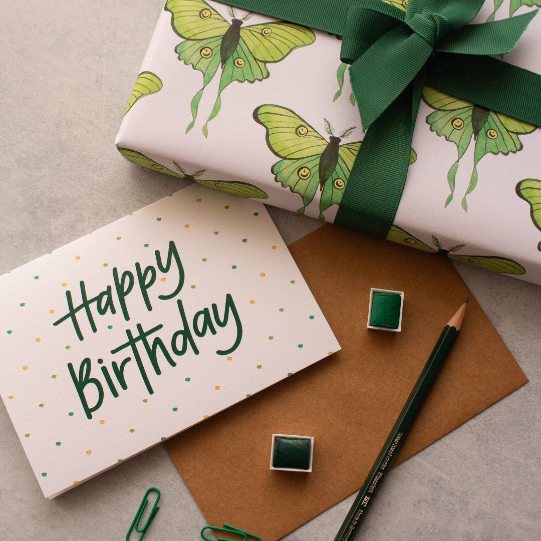 Happy Birthday card with yellow, green, and blue dots, displayed next to luna moths wrapping paper, perfect for a fun celebration.