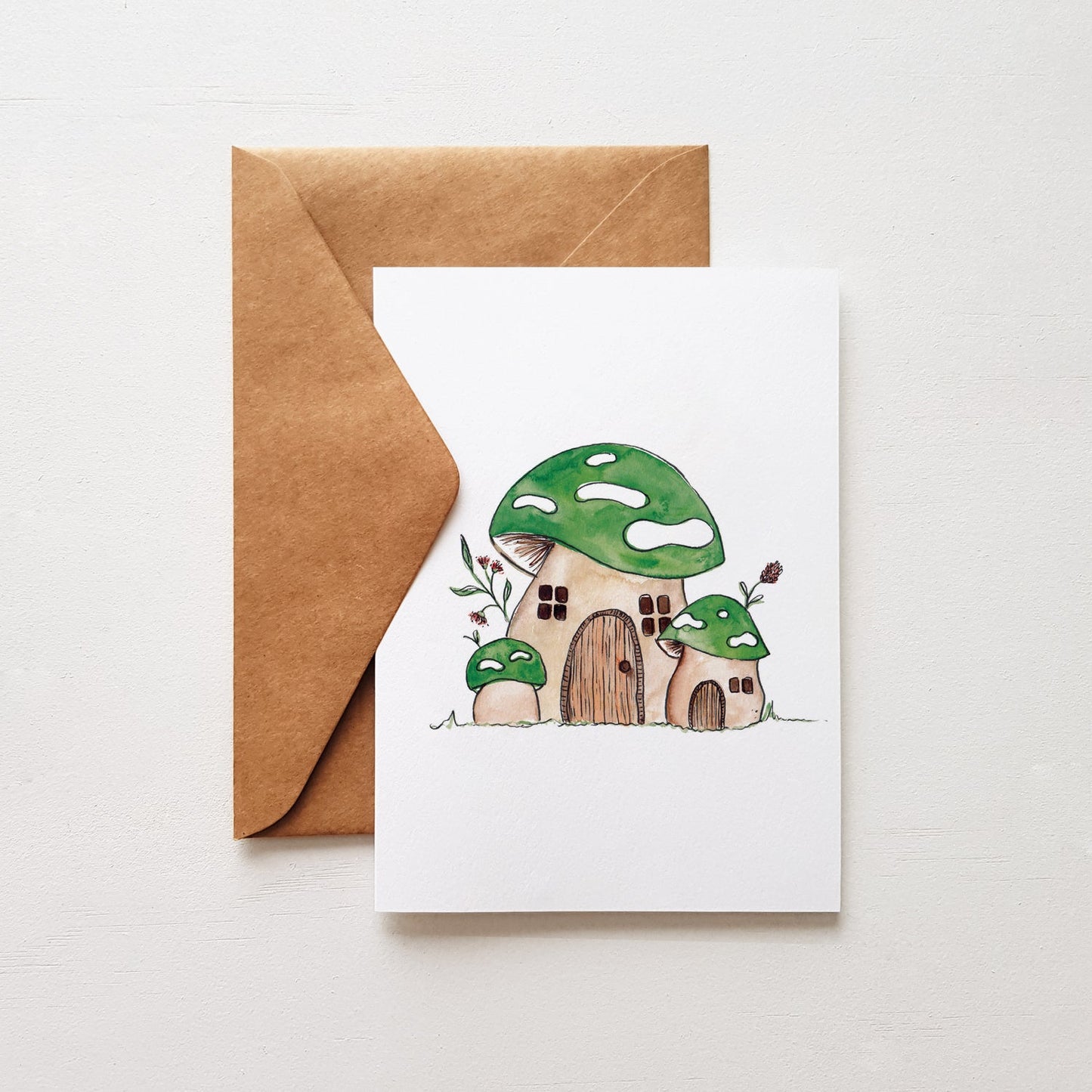House warming card with a green mushroom illustration ith a kraft envelope on a white background