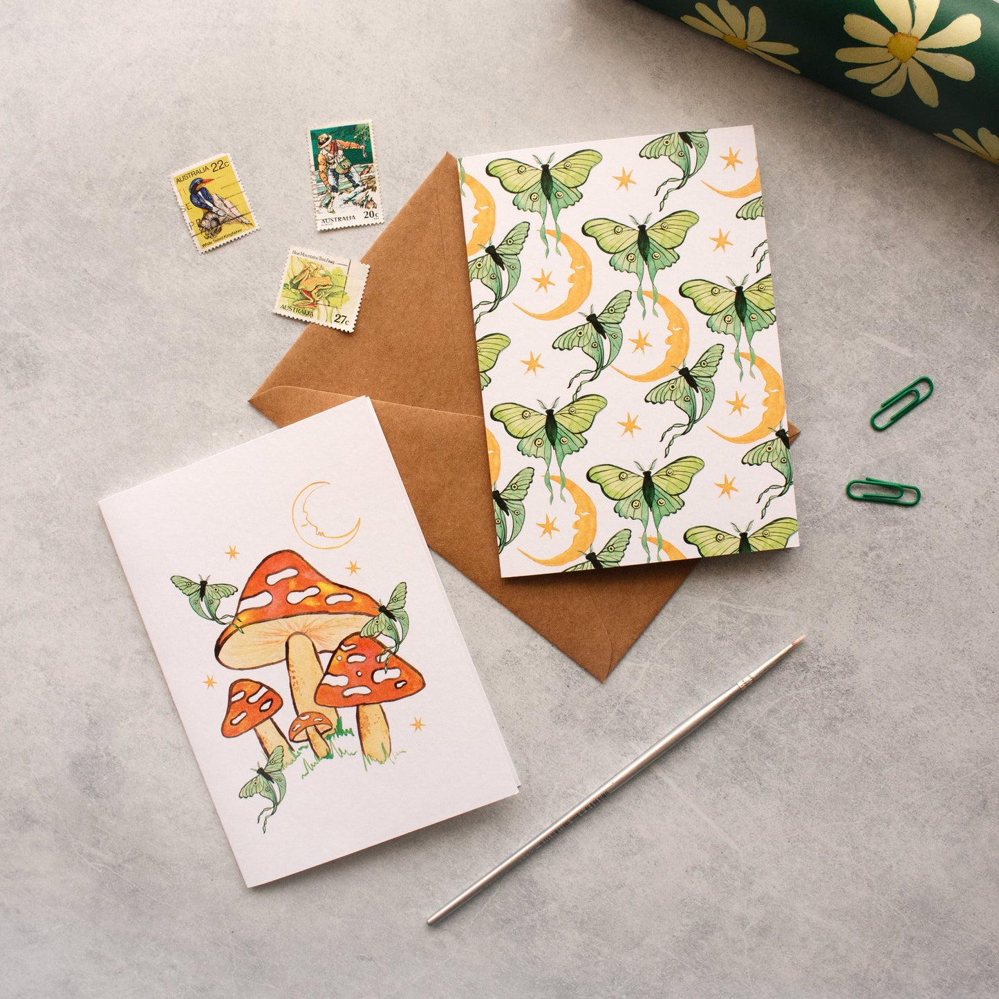Two greeting cards with different designs on a grey surface with stationery items.