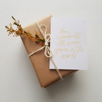 Greeting card with text 'how wonderful life is now you're in the world' in yellow on a brown present