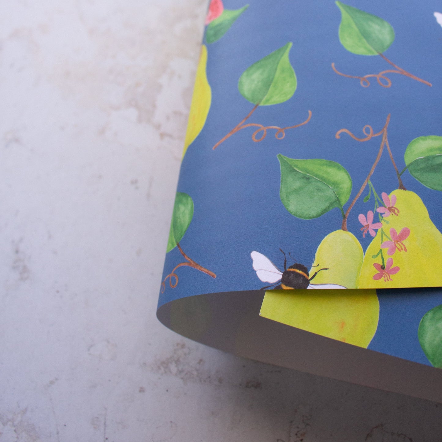 Close up image of a large sheet roll of paper with green pears, little pink flowers, dark green leaves on a blue background