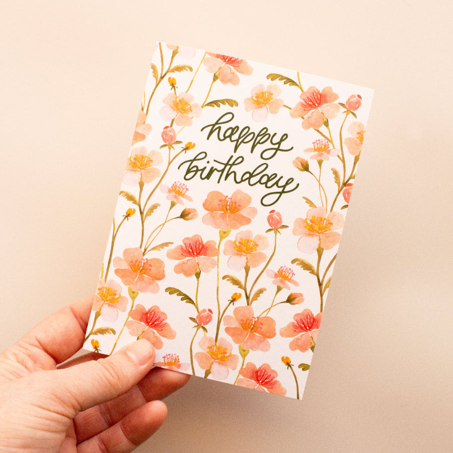 Hand holding a floral birthday card with 'happy birthday' text on a beige background