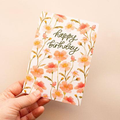 Hand holding a floral birthday card with 'happy birthday' text on a beige background