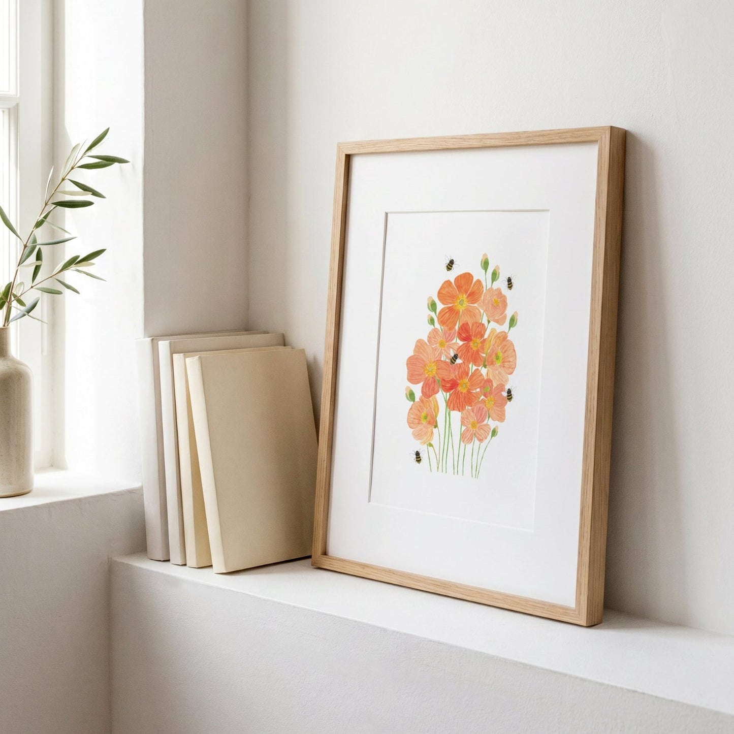A framed watercolor art print of orange poppies with green stems, displayed on a white windowsill next to a stack of neutral-colored books and a small plant in a vase.