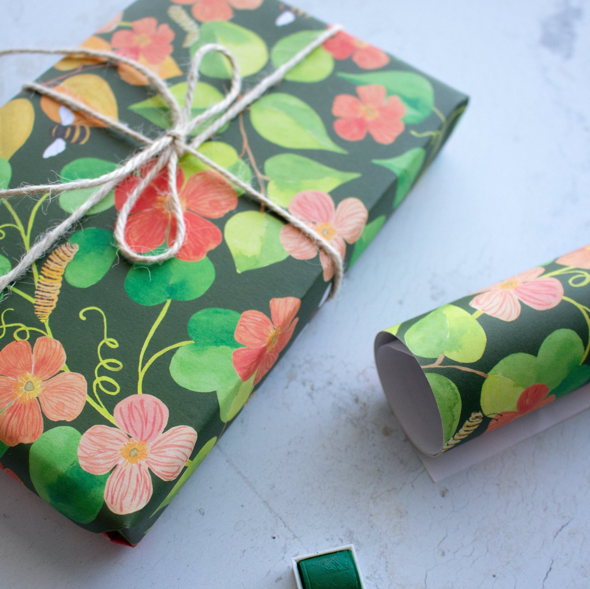 wrapped present tied in brown string next to rolled single sheet of gift wrap