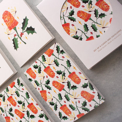 Set of Christmas-themed greeting cards with floral and holly designs on a grey surface.