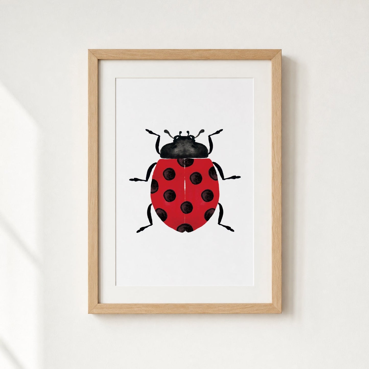 Framed artwork of a red ladybug with black spots on a white background