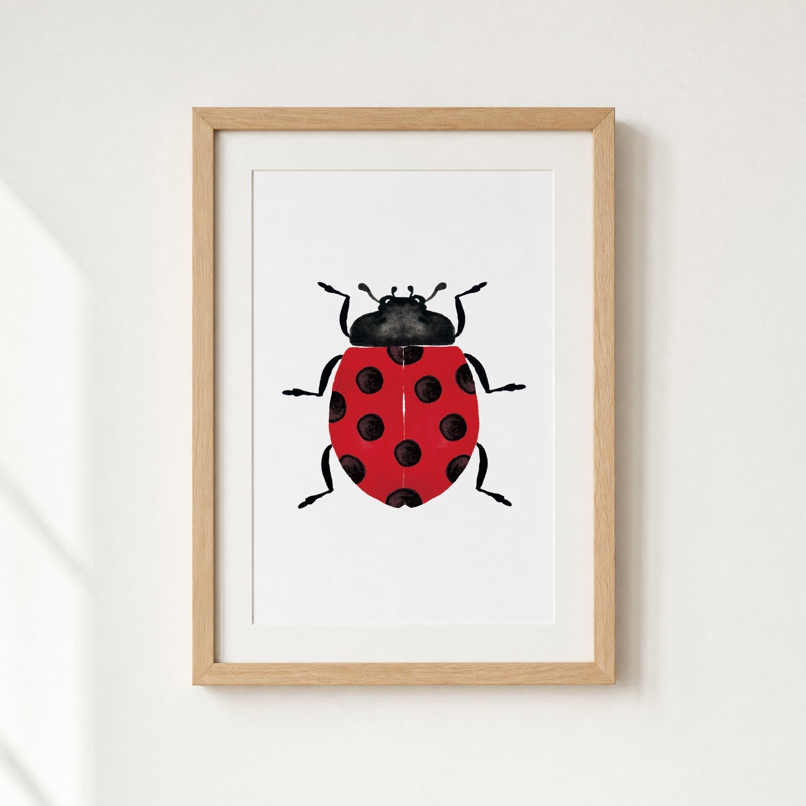 Framed artwork of a red ladybug with black spots on a white background