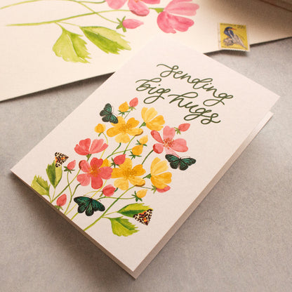 Greeting card with floral design and text 'Sending big hugs' on a grey surface.
