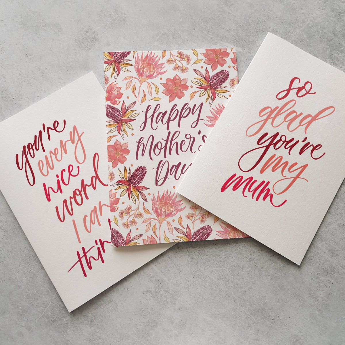 Three Mother's Day cards with floral and calligraphy designs on a grey surface.