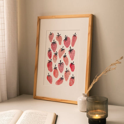 Framed original painting of pink and red strawberries, styled above a stack of books in a cozy home interior