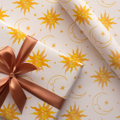 Wrapping paper featuring a celestial sun, moon, and stars design, wrapped around a gift and tied with a brown ribbon. A magical and elegant wrapping choice.