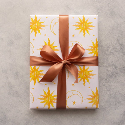 Wrapping paper featuring a repeating sun and moon pattern, elegantly tied with a brown ribbon. A celestial-inspired design perfect for gift wrapping.