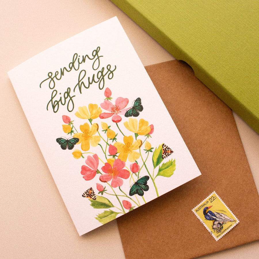 Greeting card with floral design and text 'Sending big hugs' on a beige surface with a green box.