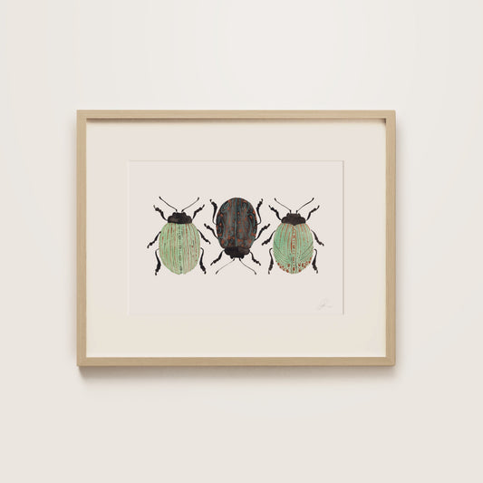 A framed art print featuring three painted beetles, housed in a light natural wood frame and mounted on a neutral off-white wall.