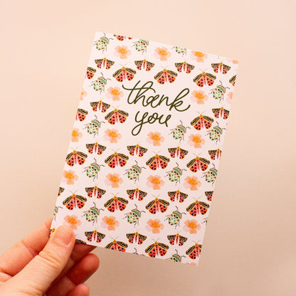 Hand holding a 'thank you' card with bug pattern on a beige background