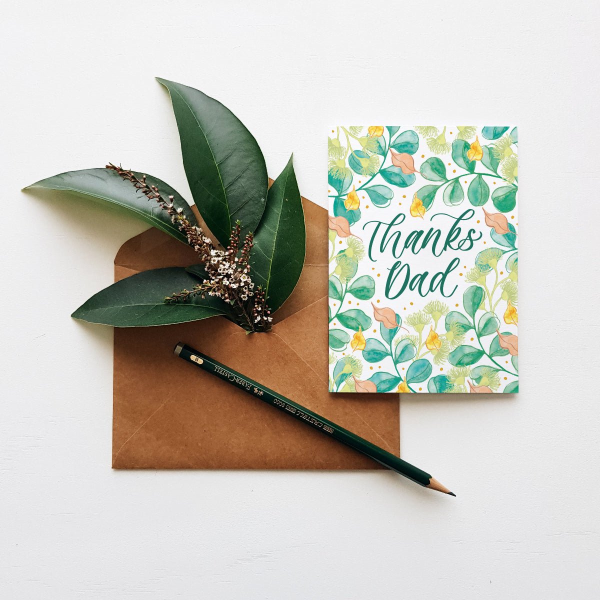 Greeting card with 'Thanks Dad' text, brown envelope, and green pen on a white background