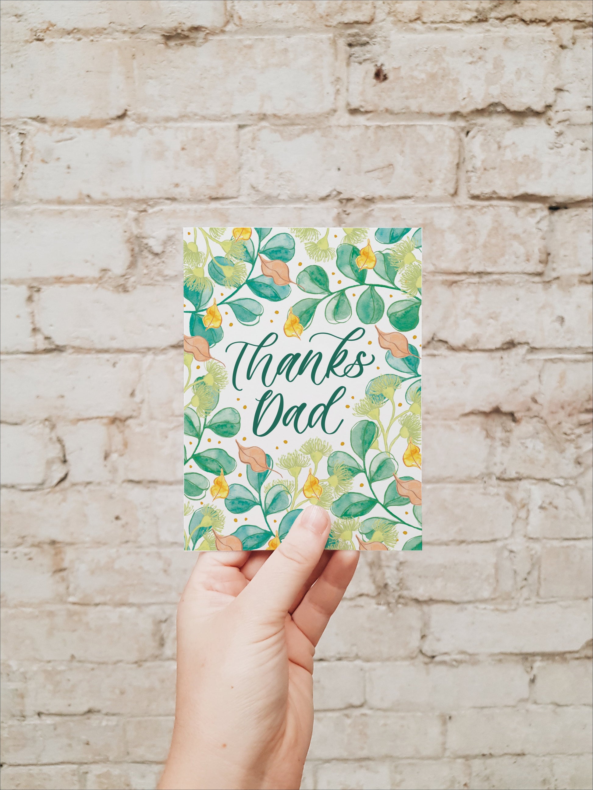 Hand holding a card with 'Thanks Dad' text against a brick wall background