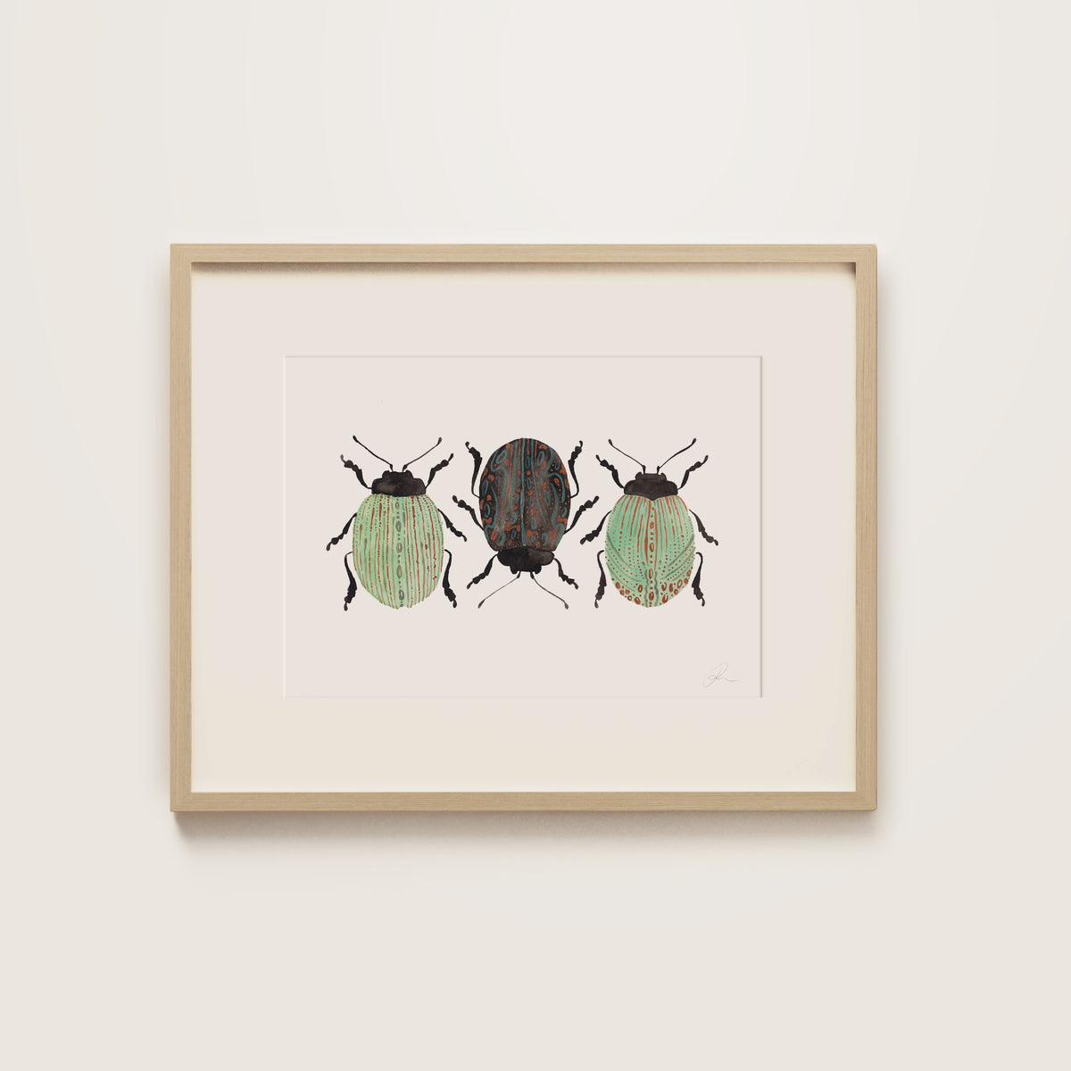 A framed art print featuring three painted beetles, housed in a light natural wood frame and mounted on a neutral off-white wall.