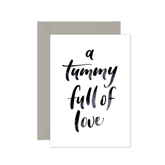 A greeting card with the phrase 'a tummy full of love' written in a cursive script, accompanied by a grey envelope, against a white background.