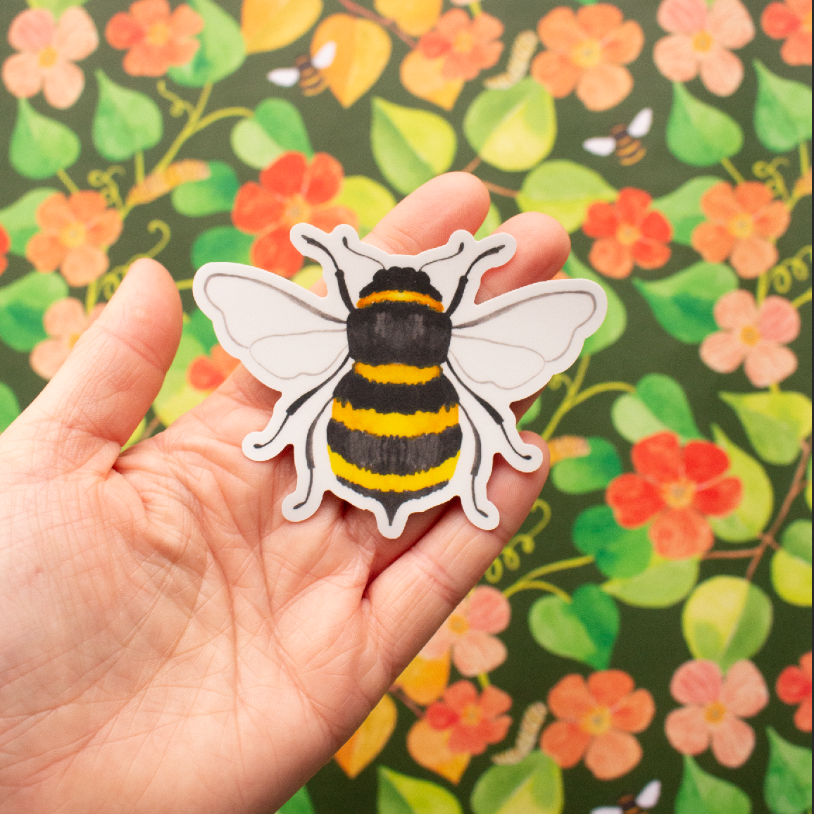 Hand holding a bee-shaped sticker against a floral background