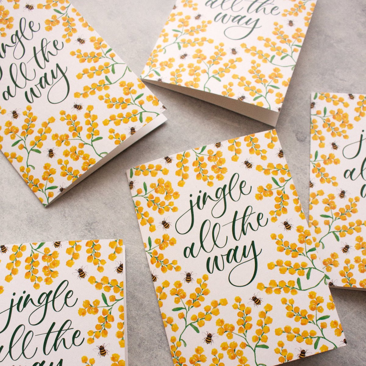 Set of greeting cards with 'jingle all the way' text and floral design on a grey surface