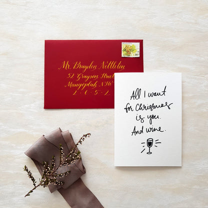 A flat-lay of a Christmas greeting card and matching red envelope with gold callirgaphy