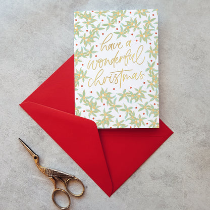 Christmas card with floral design and 'have a wonderful Christmas' text, placed on a red envelope with gold scissors beside it.