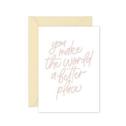 Greeting card with pink text saying 'you make the world a better place' with a cream envelope on a white background