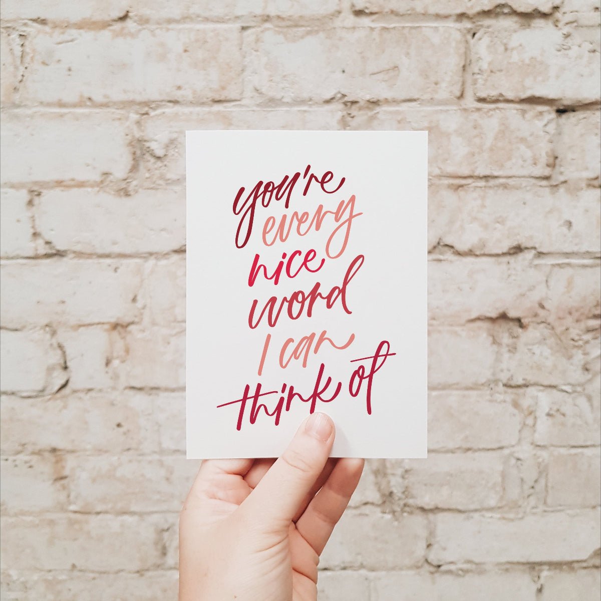 Hand holding a card with red text against a brick wall