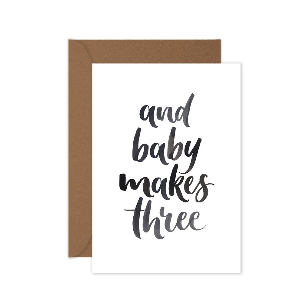 baby card with black lettering words 'and baby makes three' with a brown envelope