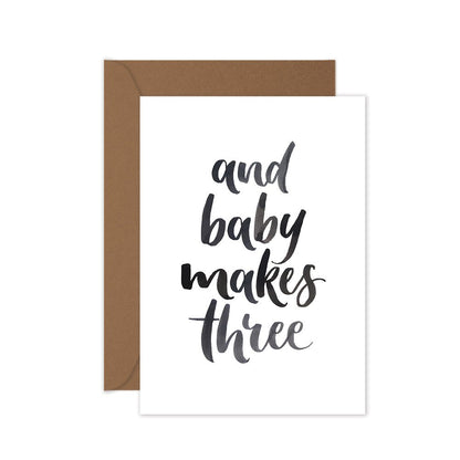 baby card with black lettering words 'and baby makes three' with a brown envelope