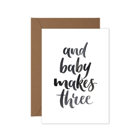 baby card with black lettering words 'and baby makes three' with a brown envelope