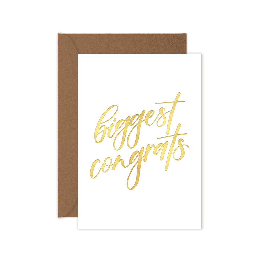 A white greeting card with 'Biggest congrats' written in gold hand lettering, accompanied by a brown kraft envelope.